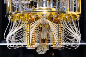 a circular structure with a shiny gold metal supports and silvery white wires runing throughout - it almost looks like a chandelier. At the very bottom there is a dark rectangle that all the wires seem to connect to, the quantum-processing chip.